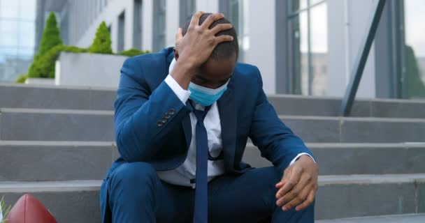 Ontslagen Afro-Amerikaanse mannelijke kantoormedewerker met medisch masker zittend op een trap in depressie met doos vol spullen. Werkloze zakenman verloor zijn bedrijf. Angstig concept. Werkloze man in wanhoop. — Stockvideo