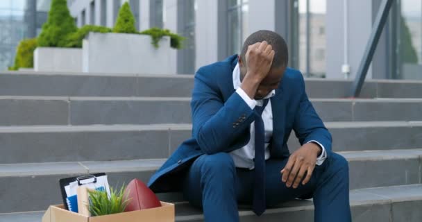 Licenziato impiegato afroamericano in giacca e cravatta seduto sulle scale in depressione con scatola di roba. L'uomo d'affari disoccupato ha perso la sua attività. Un concetto ansioso. Uomo senza lavoro nella disperazione . — Video Stock