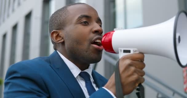 Nahaufnahme eines Afroamerikaners mit Sitz und Krawatte, der schreiend im Megafon sitzt. Männlicher Protestant, der bei einer Demonstration zu politischen oder ökologischen Themen spricht. Einzelner Protest. — Stockvideo