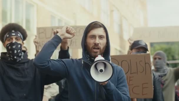 Handsome Caucasian man screaming slogans in megaphone among people against violence and police brutality outside. Strike of young male people. — Stock Video