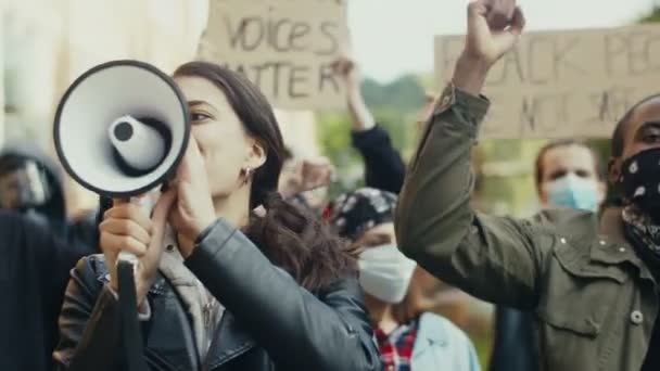 Muito jovem caucasiana gritando em megafone enquanto estava entre as pessoas em protesto contra o racismo e brutalidade policial. Manifestantes de raças mistas masculinos e femininos . — Vídeo de Stock