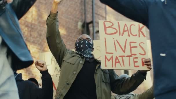 Молодые люди смешанных рас с плакатами против расизма и насилия кричат и кричат на улице в знак протеста. Протестующий афроамериканец с плакатом "Black lives Matter at street" . — стоковое видео