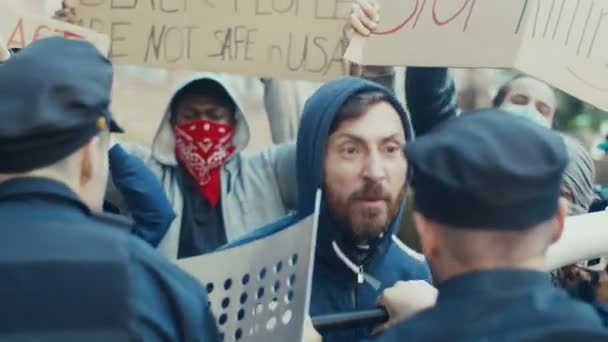 Junger kaukasischer Demonstrant schreit und schreit Polizisten bei einer Demonstration für Menschenrechte an. US-Demonstrant kämpft und streitet mit Polizisten bei Protest gegen Polizeigewalt und Rassismus. — Stockvideo