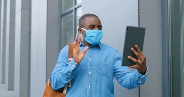 Afroamerykanin w masce medycznej stojący na ulicy i nagrywający na tablecie. Mężczyzna w ochronie dróg oddechowych jest na zewnątrz podczas rozmowy i o videochat przez kamerę internetową na komputerze. — Wideo stockowe