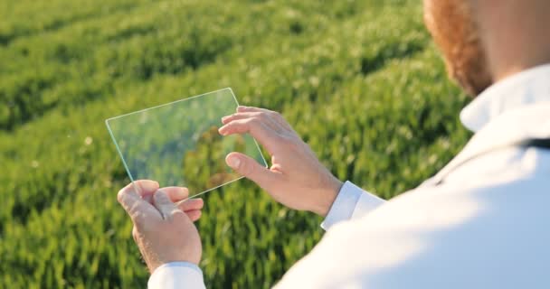 View over shoulder of male ecologist in white gown tapping on glass transparent screen. Close up of futuristic device in field. Touchscreen of hi-tech. Scientist with tablet of future in hands. — Stockvideo