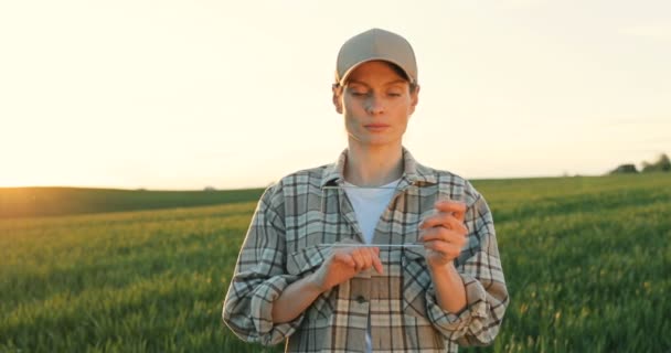 Kaukázusi fiatal vonzó nő kalapban áll zöld mezőn, üvegre koppint, mint egy futurisztikus eszköz képernyőjén. Képernyőérzékelés. Jövőbeli technológia. Női fermer átlátszó számítógéppel — Stock videók