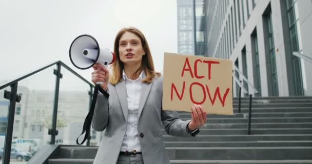 Kaukasische Aktivistin spricht und schreit in Megafon-Lautsprecher. Frau mit Plakat von Act Now auf einer einsamen Demonstration. Einzelner Protest im Freien vor dem Geschäftszentrum. Arbeitslosenkonzept. — Stockvideo