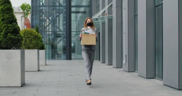 ビジネスセンターを出て踊るように物の箱で通りを歩く仮面の幸せな実業家。女性サラリーマンが仕事を辞めてお祝いする。明るい女性を解雇した。パンデミック隔離. — ストック動画