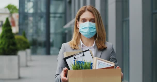 Portrait of Caucasian sad businesswoman in medical mask standing outdoor with box of stuff. Leaving business. Female office worker lost her job. Unemployment rate growing. Fired upset desperate woman. — Stock Video
