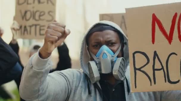 Primer plano de un joven afroamericano con capucha y máscara de gas protestando contra el racismo y gritando consignas. Al aire libre. Tipo en respirador en manifestación contra la policía . — Vídeo de stock