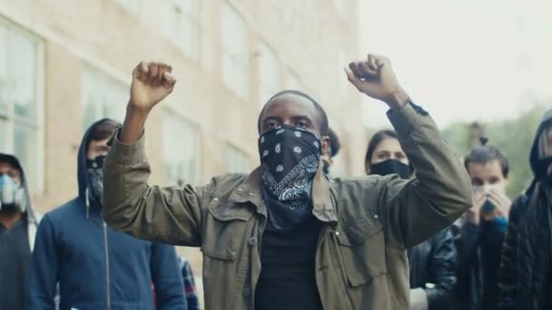 Afroamerikansk ung stilig kille i halsduk i ansiktet protesterar mitt i multietnisk skara av potestrar och skrikande motton. Killen som leder manifestationen för de mänskliga rättigheterna. — Stockvideo