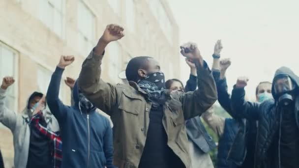 African American young handsome guy in scarf on face protesting in middle of multiethnic crowd of potesters and screaming mottos. Guy leading at manifestation for human rights. — Stock Video