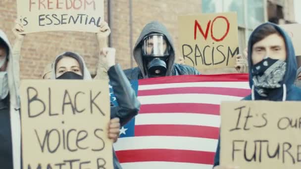 Афроамериканские и кавказские мужчины в респираторах и масках с американским флагом, выкрикивающими лозунги и участвующими в демонстрации за права и равенство чернокожих людей. Манифест в США . — стоковое видео
