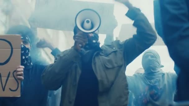 Ein junger, gut aussehender afroamerikanischer Mann mit Schal im Gesicht protestiert inmitten der Menge der Demonstranten und schreit Parolen in Megafon. Guy führt bei Demonstration und Aufruhr für Menschenrechte in Rauch auf. — Stockvideo