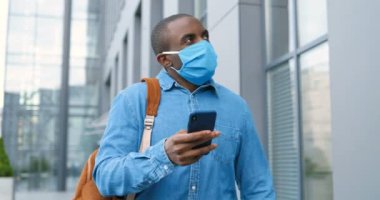 Tıbbi maskeli bir erkek yaya sokakta yürüyor, adres ve telefonla mesaj arıyor. Solunum koruma hizmetinde olan Afrikalı Amerikalı bir adam akıllı telefondan geziniyor, tıklıyor ya da kaydırıyor..