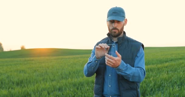 夏に緑のフィールドに立つ男性の農家の手にガラス未来的なスマートフォン。透明デバイスのハイテク技術。未来の電話でタッピング男。拡張現実. — ストック動画