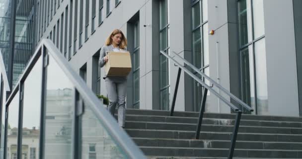 Kaukasiska upprörd affärskvinna går ner för trappan utomhus med låda med saker som lämnar businesscenter. Kvinnlig kontorsanställd förlorade sitt jobb. Arbetslösheten ökar vid virusutbrott. Avskedad kvinna — Stockvideo
