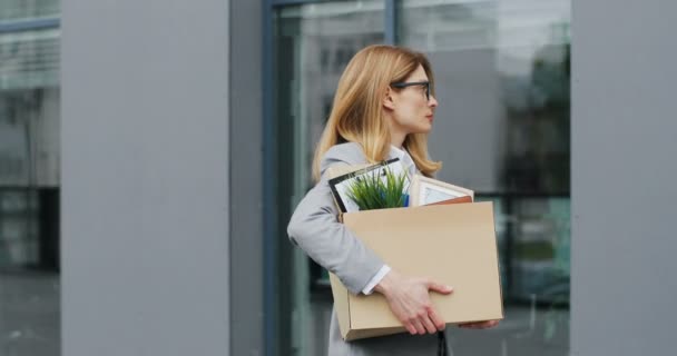 백인 여직원 이 물건 상자를 들고 사무실을 나와서 밖을 걷고 있는데. 여성 사무직 근로자는 직장을 잃었다. 세계적으로 실업률 이증가 하고 있습니다. 불타는 여자 가 집에 오고 있어. — 비디오