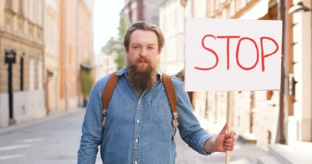 Retrato de ativista caucasiano do sexo masculino com a barba segurando cartaz Pare em manifestação política ou ambiental solitária na cidade. Um único protesto lá fora. Conceito de ativismo. Homem protestando sozinho . — Vídeo de Stock