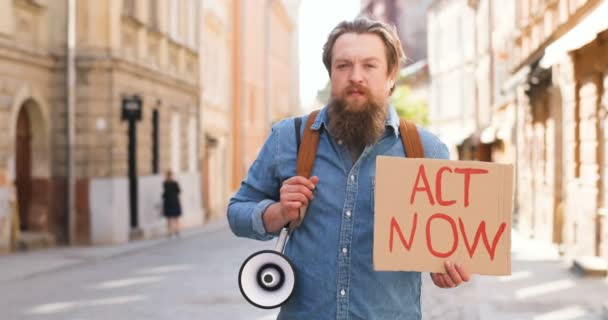 Ritratto di attivista maschio caucasico con barba che tiene poster Act ora e megafono alla manifestazione politica o ambientale solitaria in città. Una sola protesta fuori. L'uomo che protesta da solo . — Video Stock