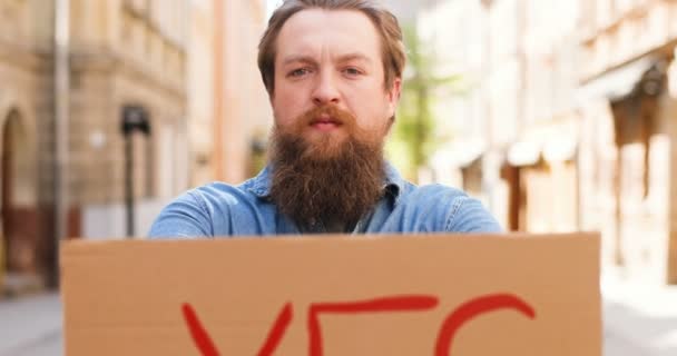 Närbild av vit ung man står utomhus i stan och visar bord Ja ord. Man demonstrera styrelse och affisch med överenskommelse uttalande. — Stockvideo