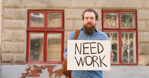 Portretfoto van werkloze blanke jongeman die op straat staat in de stad en affiche toont met Need Work woorden. Mannelijk werkloos demonstratiebord met aankondiging. Werkloze na sluiting. — Stockvideo