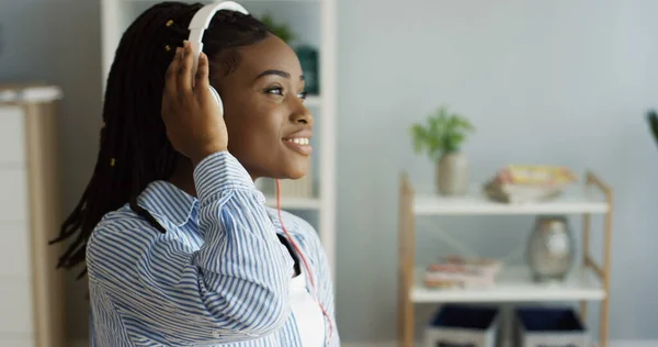 Lähikuva söpö Afrikkalainen amerikkalainen nainen saparot ja iso valkoinen kuulokkeet liikkuvat päätään, laulaa ja kuunnella musiikkia. Sisätilat — kuvapankkivalokuva