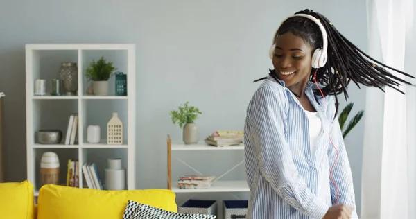 Güzel, genç, neşeli, Afro-Amerikan kadın kulaklıkla dinlediği müziğin ritmiyle dans ediyor. - Evde. İçeride.