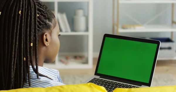 Vista sobre o ombro sobre a jovem afro-americana com tranças sentadas na frente do computador portátil aberto com tela verde e pensando. Chave Chroma. Fecha. Interior — Fotografia de Stock