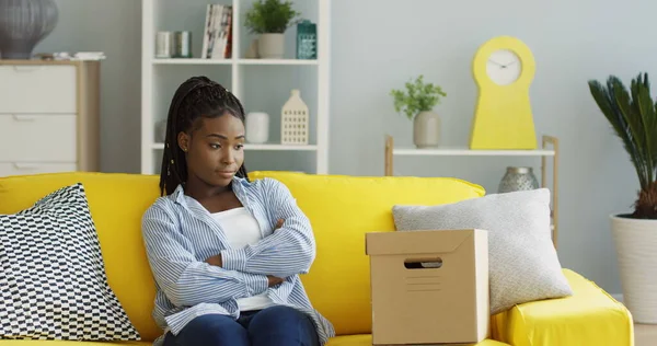 Nuori afroamerikkalainen nainen saa postipaketin, avaa laatikon, riisuu kirjavan paidan ja on tyytymätön. Sisällä — kuvapankkivalokuva