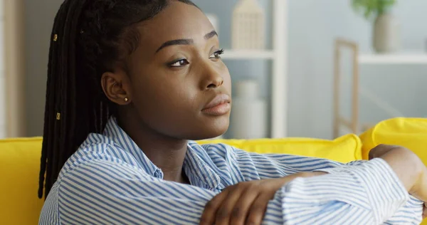 Nær den triste, deprimerte afroamerikanske unge kvinnen som sitter på sofaen og tenker. Innvendig stockfoto