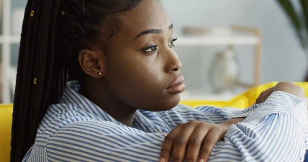 รูปภาพของหญิงสาวชาวแอฟริกันอเมริกันที่อารมณ์เสีย มีอาการซึมเศร้าและนั่งบนโซฟาที่บ้าน ในร่ม รูปภาพสต็อกที่ปลอดค่าลิขสิทธิ์