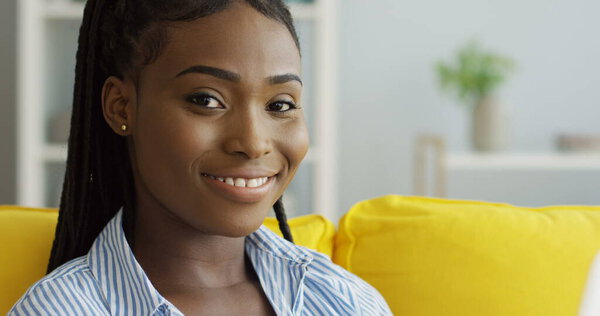 Close up of the young African American woman typing on the keyboard of the laptop computer at home on the yellow couch. Indoor Royalty Free Stock Photos