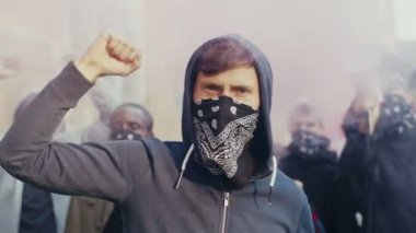 Kapüşonlu ve eşarplı beyaz yakışıklı delikanlıyı dışarıda duman ve gaz içinde sloganlar atarken ve bağırırken yakalayın. ABD 'de sokağa saldıran çok ırklı adamlar.