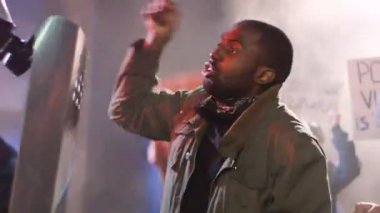 Gece vakti erkek protestocular tam teçhizatlı kostümlerle polisle kavga edip kavga ederken sokak kavgası. İsyanda duman içinde dururken polise bağıran Afro-Amerikalı bir adam. Saldırgan adam..