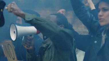 Erkek ve kadın çoklu etnik gruplar ABD 'de ırkçılık ve polis eylemlerini protesto etmek için slogan atıyorlar. Afro-Amerikalı adam megafonla lider ve bağırıyor ve beyaz kız posterini tutuyor..
