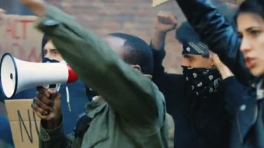 Erkek ve kadın karışık ırk öncüleri, ABD 'de ırkçılık ve polis eylemlerini protesto etmek için slogan atıyorlar. Afro-Amerikalı adam megafonla lider ve bağırıyor ve beyaz kız posterini tutuyor..
