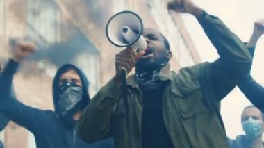 Afro-Amerikalı genç adam Amerika 'da ırkçılığı protesto etmek için sokak ortasında megafonla ve sigara içerek slogan atıyordu. Saldırgan çoklu etnik isyancılar taleplerini haykırıyorlar..