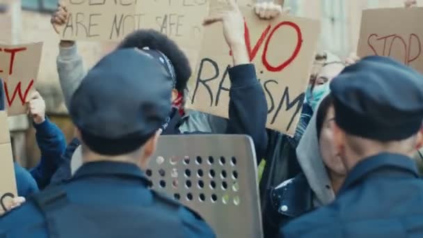 若い多民族の男性と女性の学生は、暴力や人種差別に対する抗議で警察と戦い、口論する米国の抗議者のためのデモで警察に叫び、叫んでいます — ストック動画