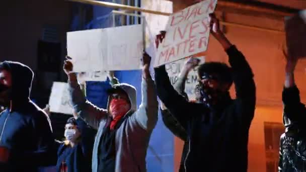 Manifestantes masculinos multiétnicos com rostos mascarados segurando cartazes contra o racismo e a agressão policial à noite. Protesto de rebeldes de raças mistas nos EUA. Manifestação no conceito de noite . — Vídeo de Stock