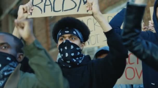 Close up de mestiços jovens estudantes do sexo masculino e feminino com máscaras nos rostos em pé na multidão com cartazes e protestando contra o racismo e a violência. Multiétnica multidão em manifestação nos EUA . — Vídeo de Stock