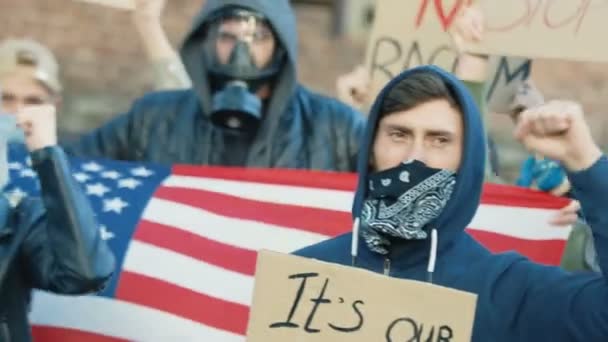 Manifestantes masculinos jóvenes multiétnicos con máscaras y respiradores protestando contra el racismo y los actos ilegales de la policía. Rebeldes de razas mixtas con carteles y bandera americana. Hombres gritando consignas en la calle . — Vídeos de Stock