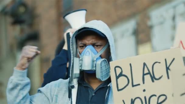 Manifestantes masculinos jóvenes multiétnicos con máscaras y respiradores protestando contra el racismo y los actos ilegales de la policía. Rebeldes de razas mixtas con carteles y bandera americana. Hombres gritando lema Las voces negras importan — Vídeos de Stock