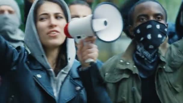 Caucasian young woman leader screaming mottos in megaphone at street in crowd and smoke at protest against racism in USA. Active mixed-races protesters shouting demands. Female leading at rebellion. — Stock Video