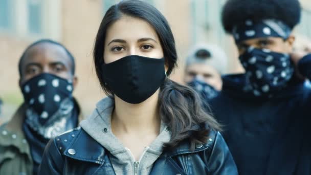 Sokak ayaklanmasında, maske takmış genç beyaz bir kadının kameraya bakışını yakından çek. Arkasında erkek Afro-Amerikan olan bir kızın portresi. Gösteride kadın protestocu. — Stok video