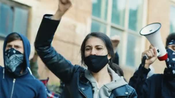 Beautiful Caucasian young woman in mask screaming mottos at protest in multiethnic male crowd. Female pretty protester at manifestation for human rights and against police violence shouting slogans. — Stock Video
