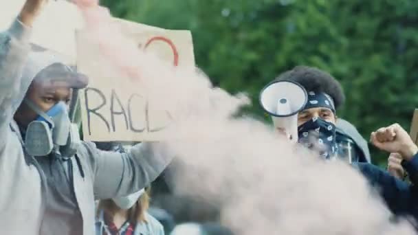 Hombres de razas mixtas manifestantes en respiradores y máscaras protestando con humo colorido y carteles contra el racismo y la brutalidad policial en Estados Unidos. Hombres multiétnicos luchando por la igualdad de derechos en disturbios callejeros . — Vídeos de Stock