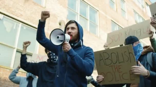 Лидер кавказской молодежи кричит лозунги в мегафоне на улице в толпе в знак протеста против расизма в США. Активные протестующие смешанных рас выкрикивают требования. Мужчина, ведущий восстание . — стоковое видео