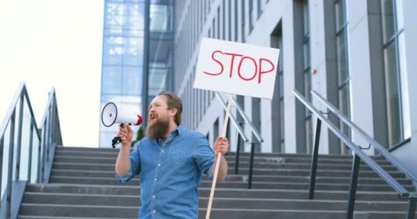 Одинокий протест кавказького чоловіка з бородою говорить і кричить мегафоном. Чоловіки, які протестують, тримають стіл "Стоп", привертаючи увагу до політичних або екологічних питань. Самотні протести. — стокове відео