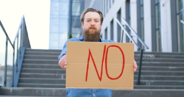 Porträtt av vit manlig aktivist med skägg innehar affisch nr vid demonstration eller protest. En enda protest utomhus. Begreppet förnekande av aktivism. Mannen som visar bord med ord nr. Avslag. — Stockvideo